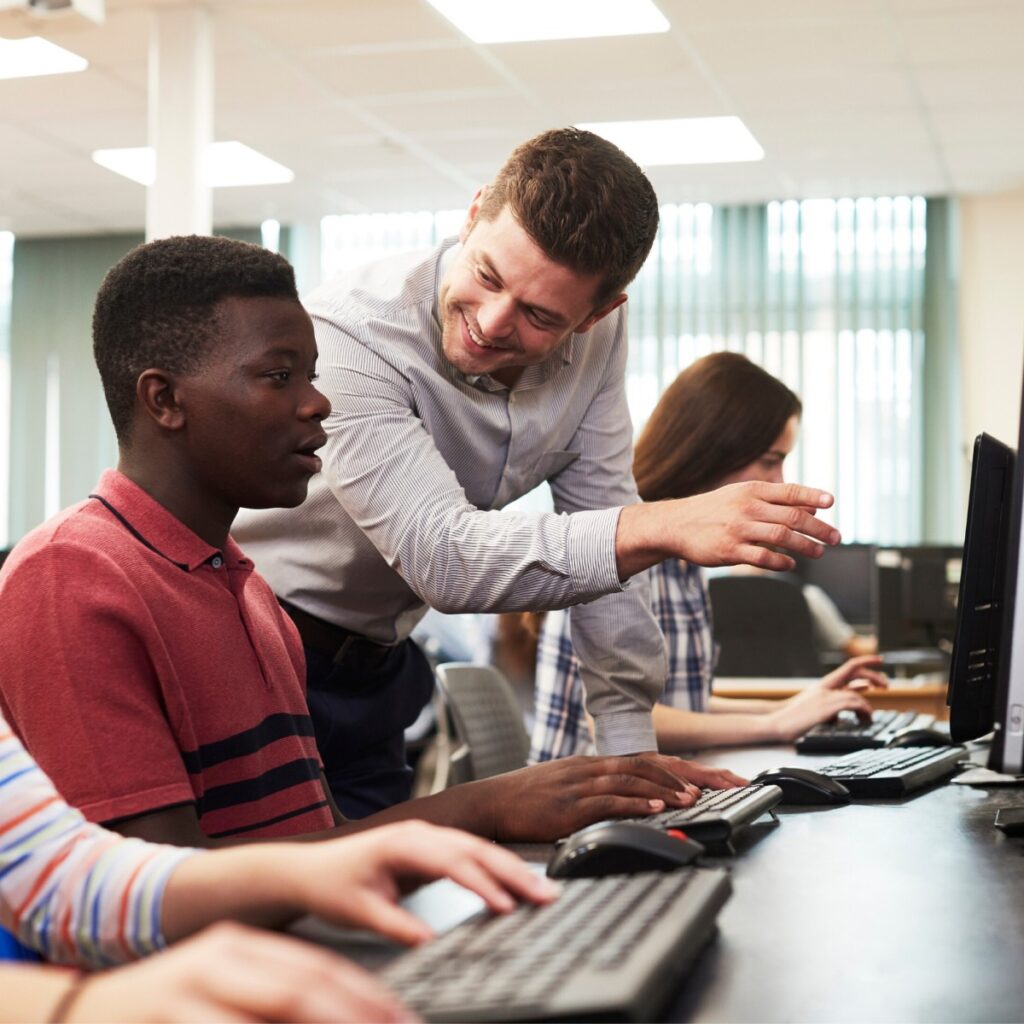 Academies - Teacher helping students at computers