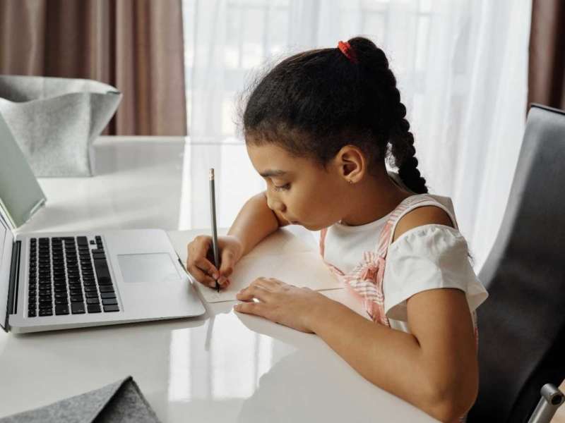 Child writing while working on laptop