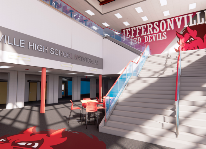 Interior of a high school atrium featuring a sign reading '... High School Natatorium', a red devil mascot mural on the wall, a wide staircase with glass railings, and a round table with red chairs nearby.